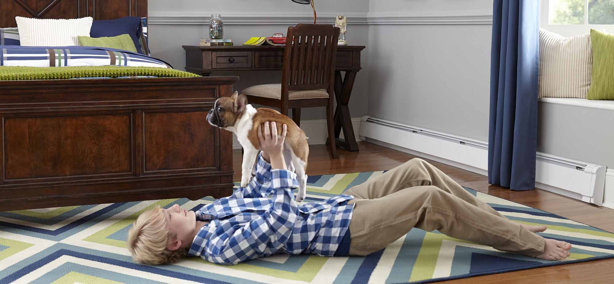 Imagen de un niño tendido en el suelo jugando con su perrito, disfrutando del cálido y confortable ambiente que le brindan los Zoclo Térmicos de Slant/Fin.